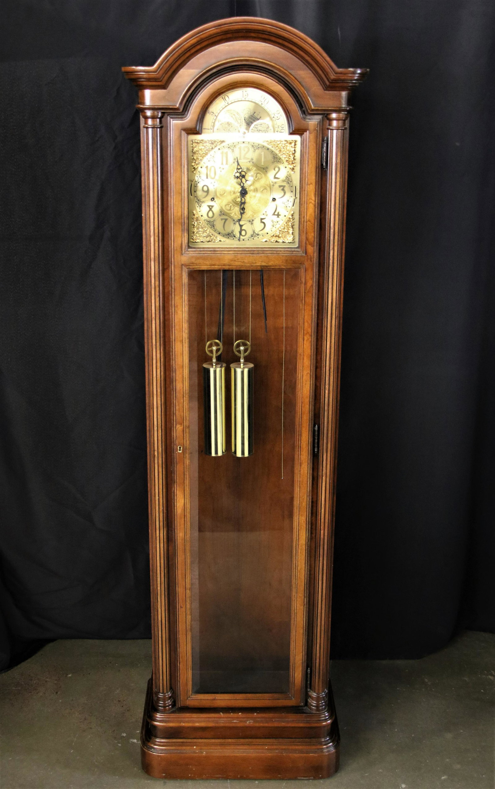Howard Miller, Grandfather Clock: Wooden grandfather clock; Glass front door houses gold toned pendulum and weights; Moon phase dial featured above clock face; Measures approximately H80 x W 23 x D 14 inches; Right weight and pendulum