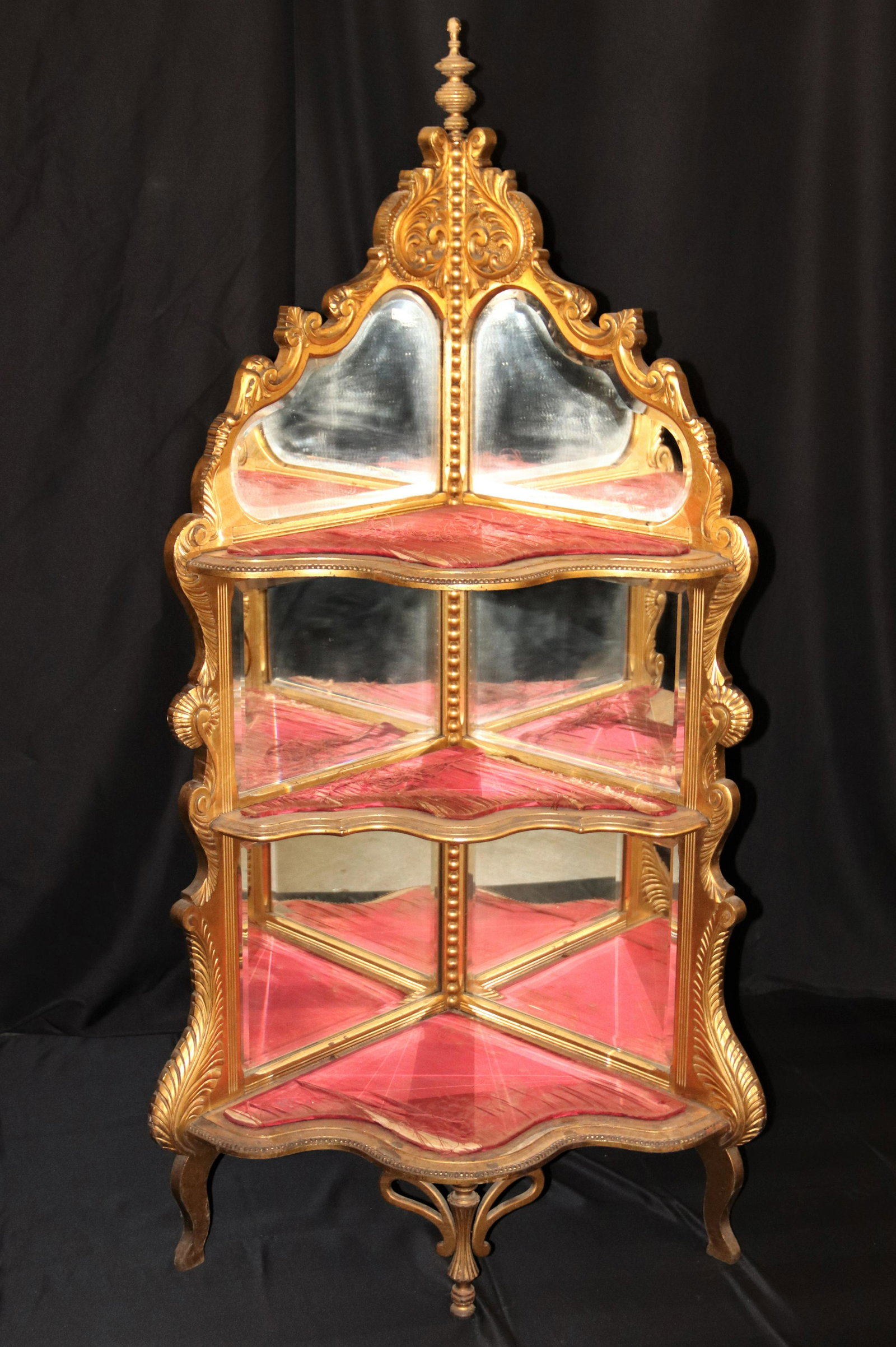 Gold Gilded Corner Cabinet: Corner cabinet gold gilded with three upholstered shelves and mirrored backs; Measures approximately H 64 x W 32 1/2 x D 19 1/2 inches; Gold on finial is flaking; Upholstery is shredded in some places
