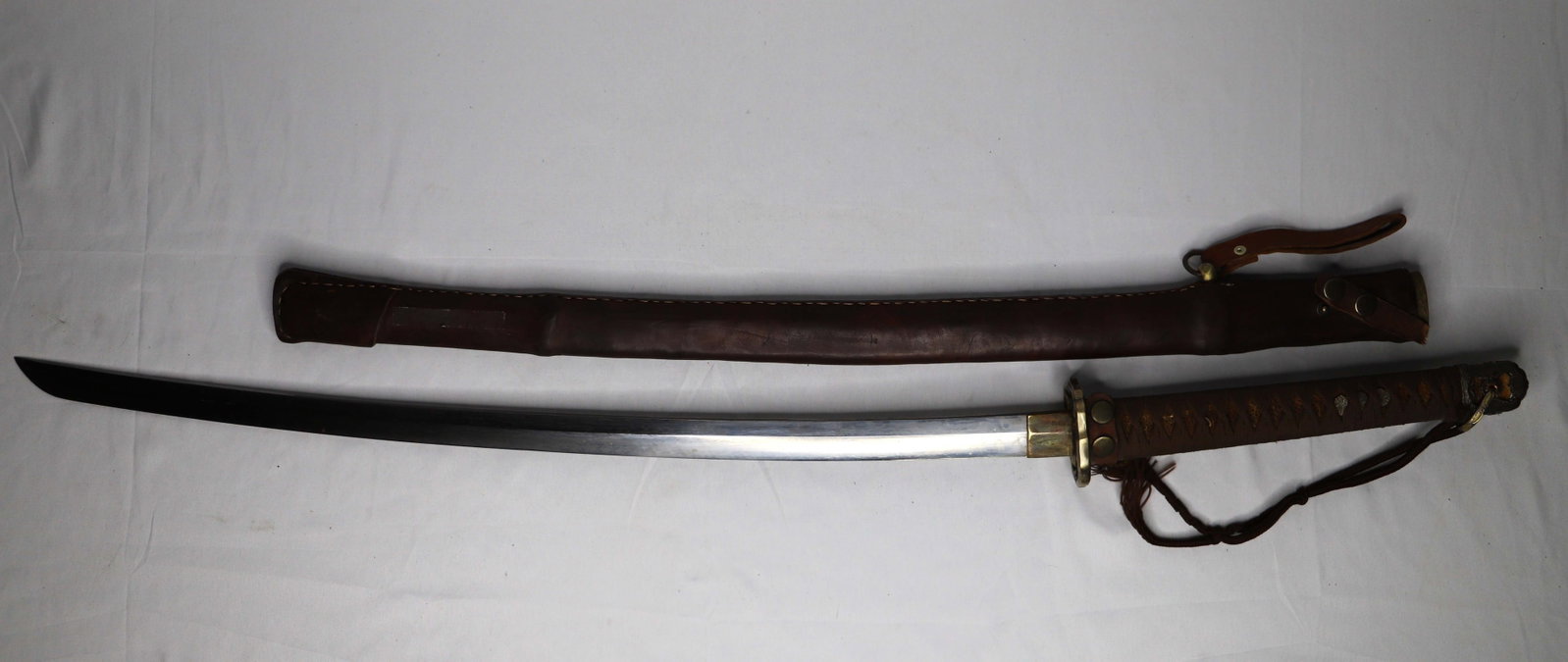 Japanese Sword: Katana style sword with leather sheath; Possibly "The Master's Sword"; No maker marks observed; Numbered "99898"; Measures approximately L 41 inches; Leather strap is broken; See photos. Pick up in De