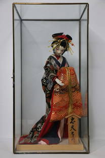 Japanese Geisha Doll: Geisha figurine has painted wood head and fabric hands; Dressed in traditional clothes and head gear; Comes in a glass display case; No maker marks observed; Case measures approximately H 20 x W 10 x