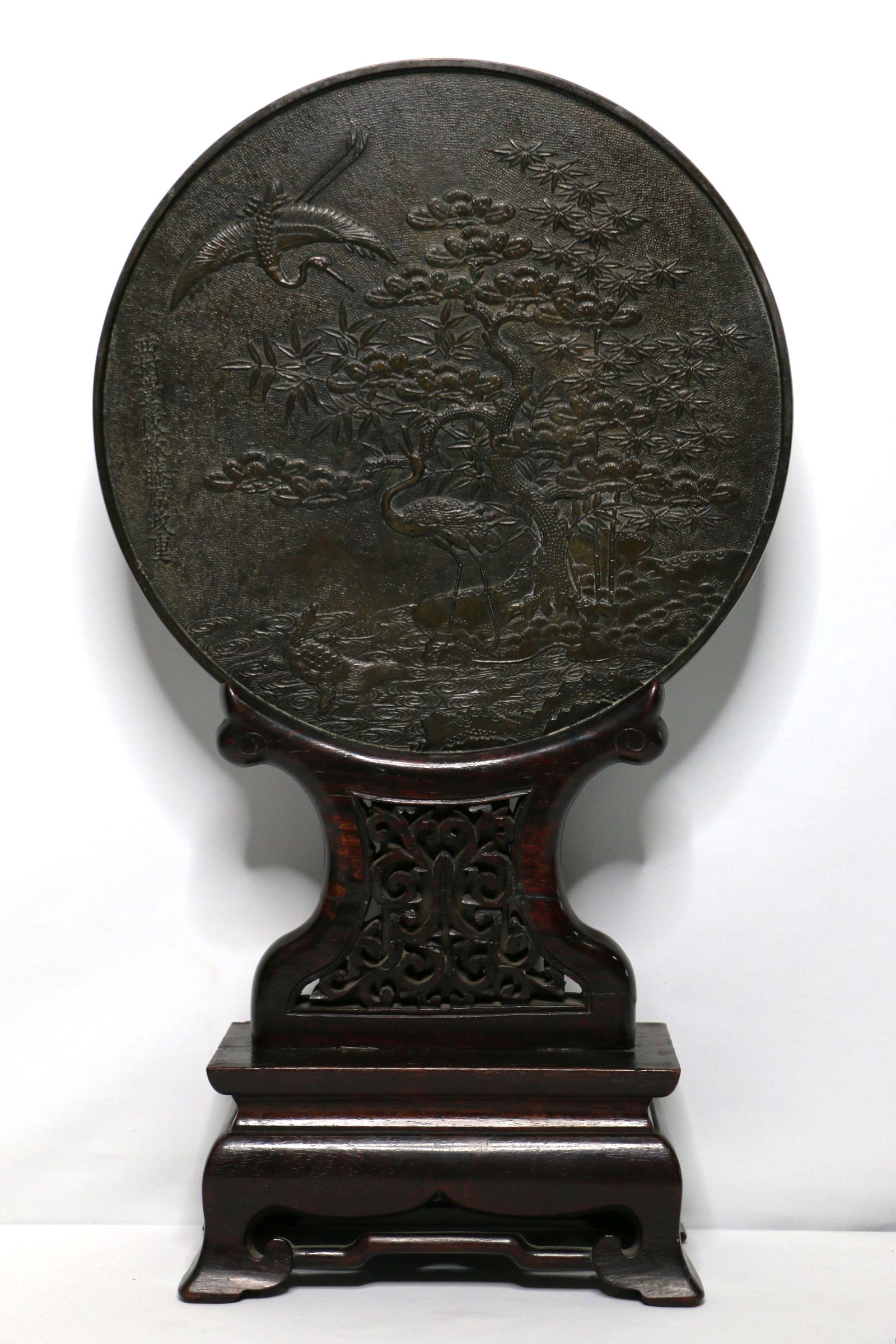 Chinese Mirror: Polished face; Reverse decorated with exotic plants, trees, cranes and turtle; On carved teak stand; Measures approximately H 19 x Diameter 11 inches; Wear commensurate with age; See photos. Pick up i