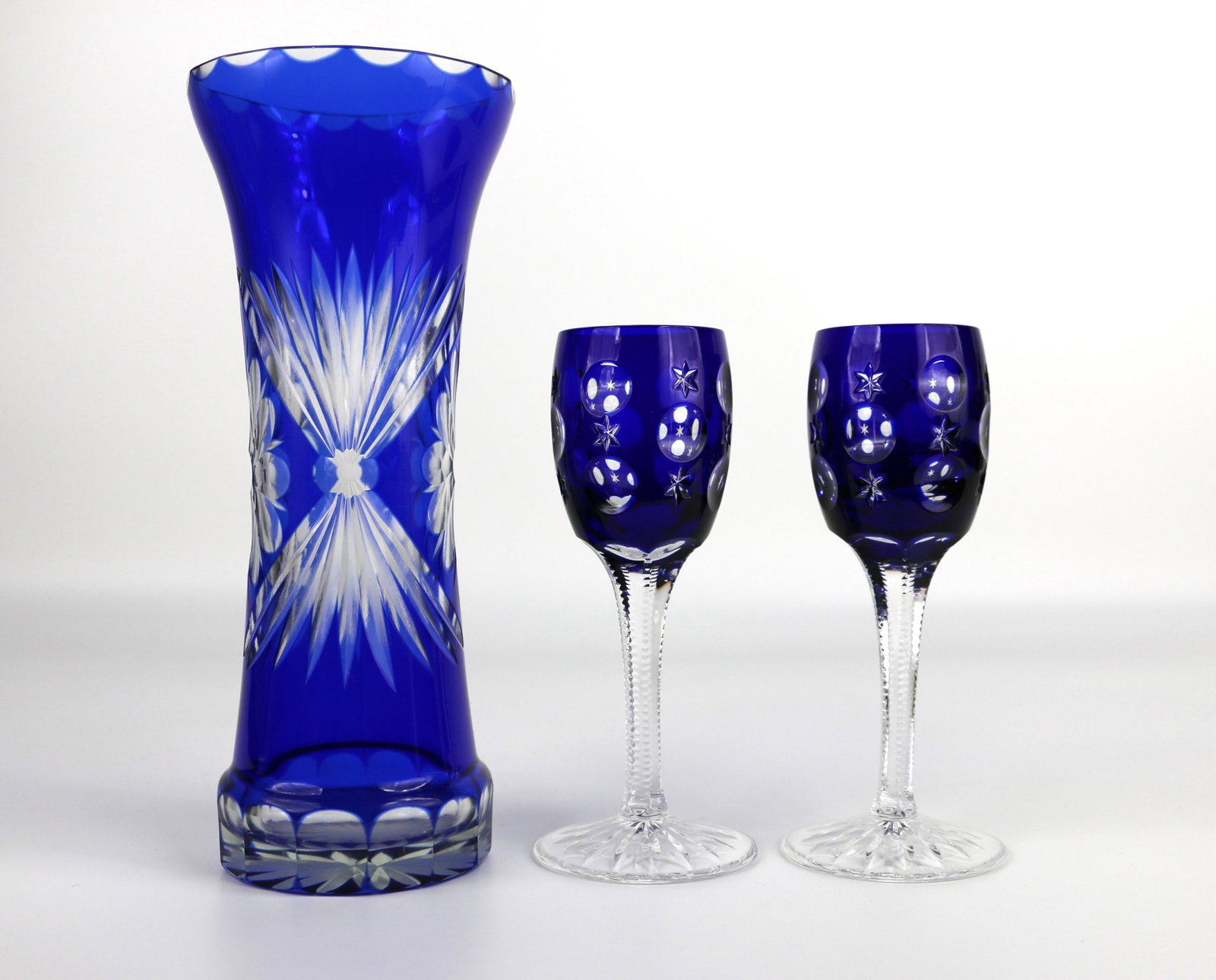 Faberge, Cut to Clear Crystal: Two blue liqueur / cordial glasses marked "Faberge" on the bottom; Blue crystal cut to clear with moons and stars; One unmarked vase; Each glass measures approximately H 5 3/4 x Diameter 1 3/4 inches;