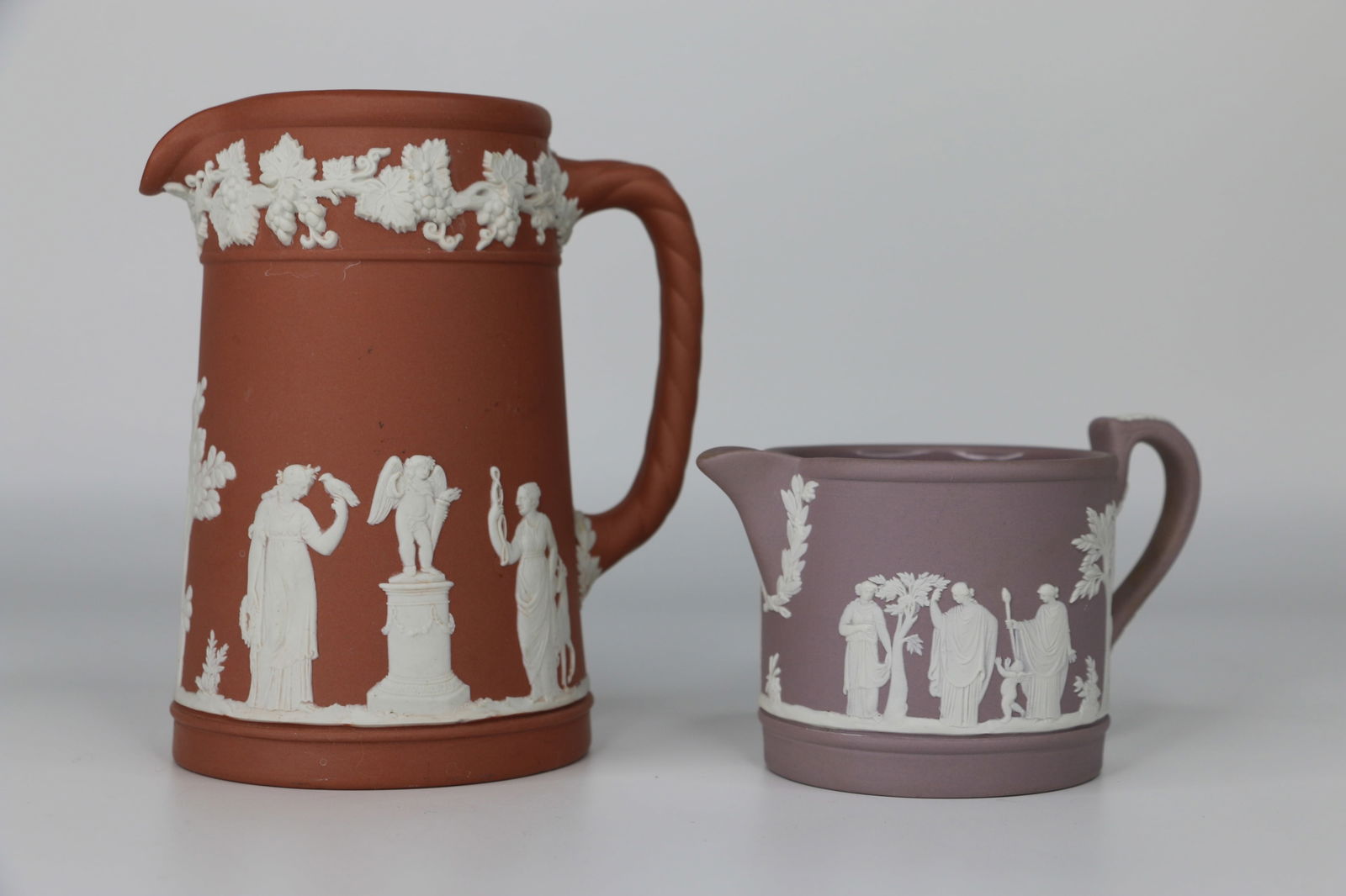 Wedgwood, Jasperware: Lilac creamer; Terracotta red pitcher; Both marked "Wedgwood, England" on the base; Creamer measures approximately H 2 1/2 x W 4 1/2 x D 2 3/4 inches; Slight scratching on red handle. See photos
