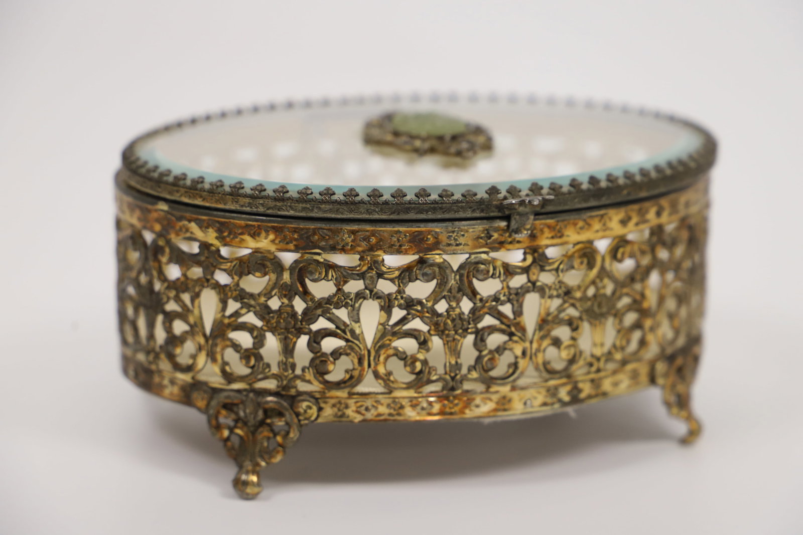 Vintage Jewelry Casket: Ormolu filigree jewelry box with beveled glass lid; Carved stone on lid is possibly jade; No maker mark observed; Measures approximately H 3 x W 6 1/4 x D 5 1/4 inches; Wear and tarnishing on the meta