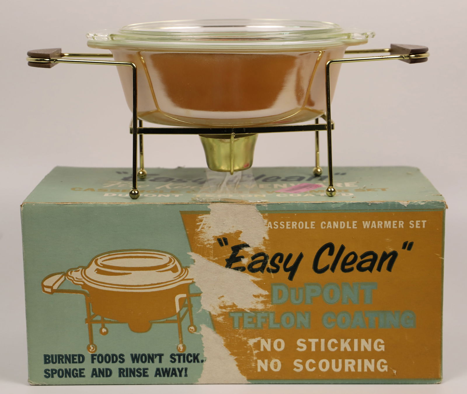 Fire King, Casserole Set: 1 1/2 quart "Easy Clean" oval casserole with cover; Sits in candle warmer with walnut handles; New in original box; Casserole with lid measures approximately H 4 1/2 x W 10 1/2 x D 7 1/2 inches; Box i