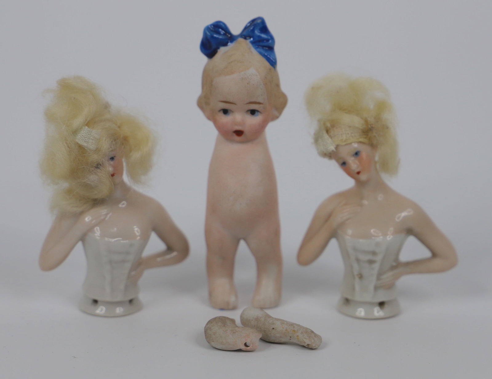 Porcelain Dolls: Two china half dolls/pin cushion dolls; Porcelain doll marked "Made in Japan"; Half dolls measure approximately H 3 x W 2 x D 1 inches; Visible discoloration on porcelain doll, arms included but not a