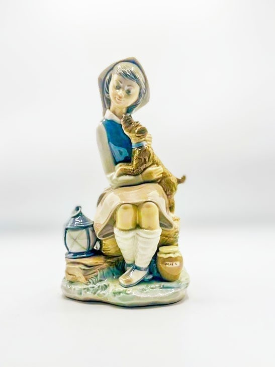 Girl with Lantern, Sabino France: This Lladró porcelain figurine depicts a young girl (wearing a bonnet/hood, blue bodice, beige skirt, white stockings, and holding a small puppy/dog) seated on a rock or log base, with a lantern and