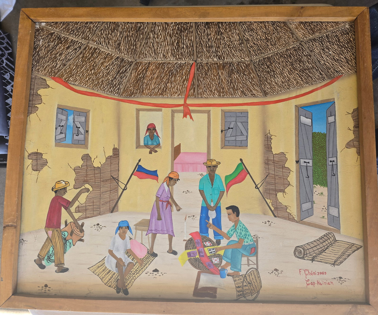 Cap-Haïtien Interior Scene by F. Chérizaad: Vibrant and detailed original painting depicting a lively scene inside a large, circular thatched-roof house (typical of rural Haitian architecture). The interior shows cracked yellow walls, open door