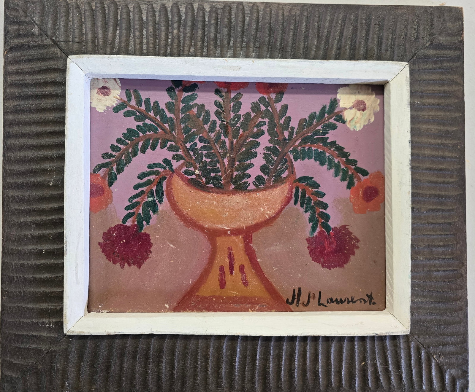 H.P. Laurent – Floral Still Life in Vase, 12 x 14 in., Bricston Collection: Charming naïve still life depicting a pedestal vase brimming with red, white, and orange flowers amid abundant green leaves, set against a soft pink background. Rendered with bold, simplified forms a