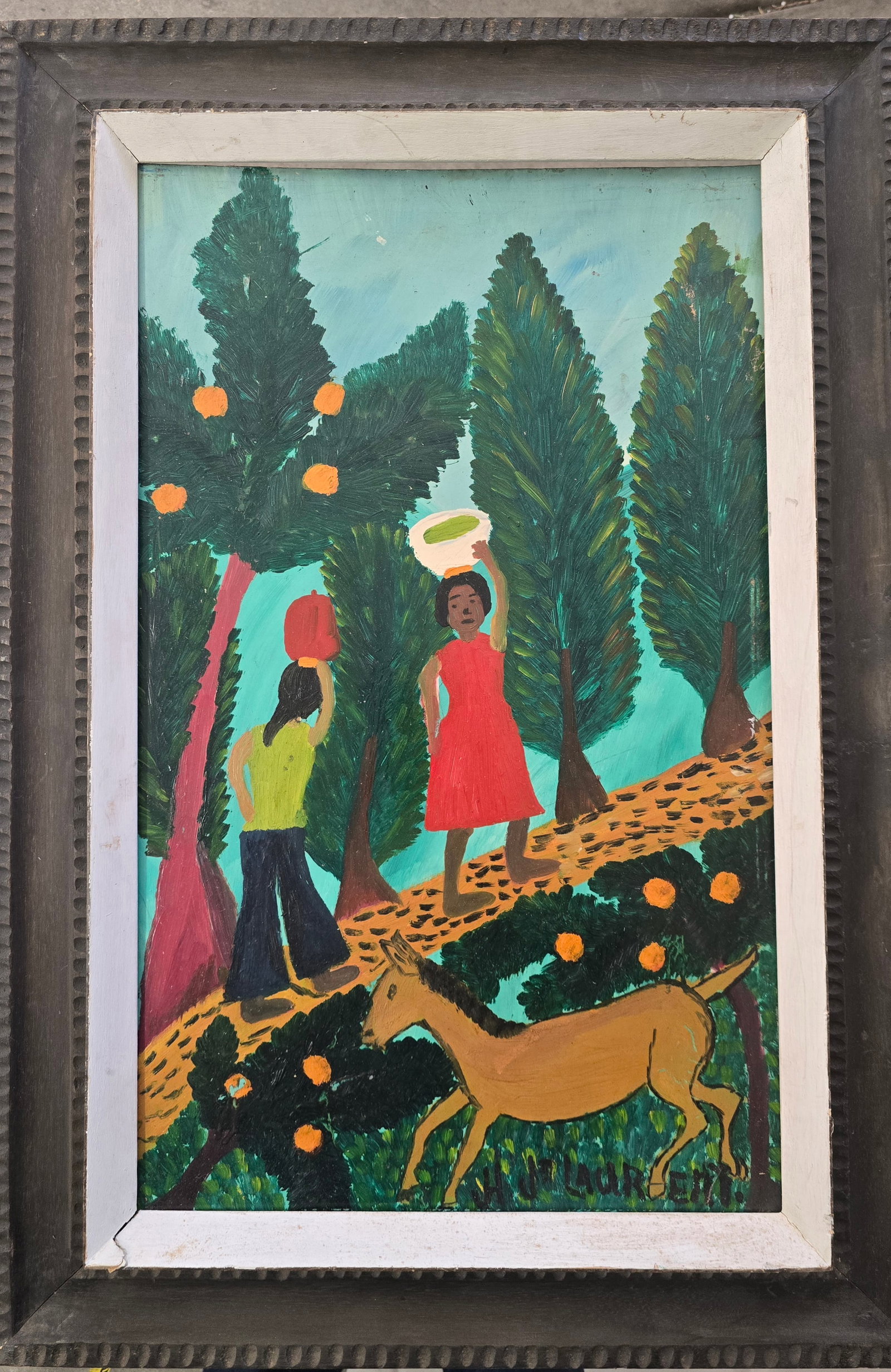 H. P. Laurent – Women on a Path with Donkey, Bricston Collection: A charming Haitian naïve painting depicting two women walking along a winding dirt path through a lush, stylized landscape. The woman in a bright red dress balances a white bowl on her head, while th