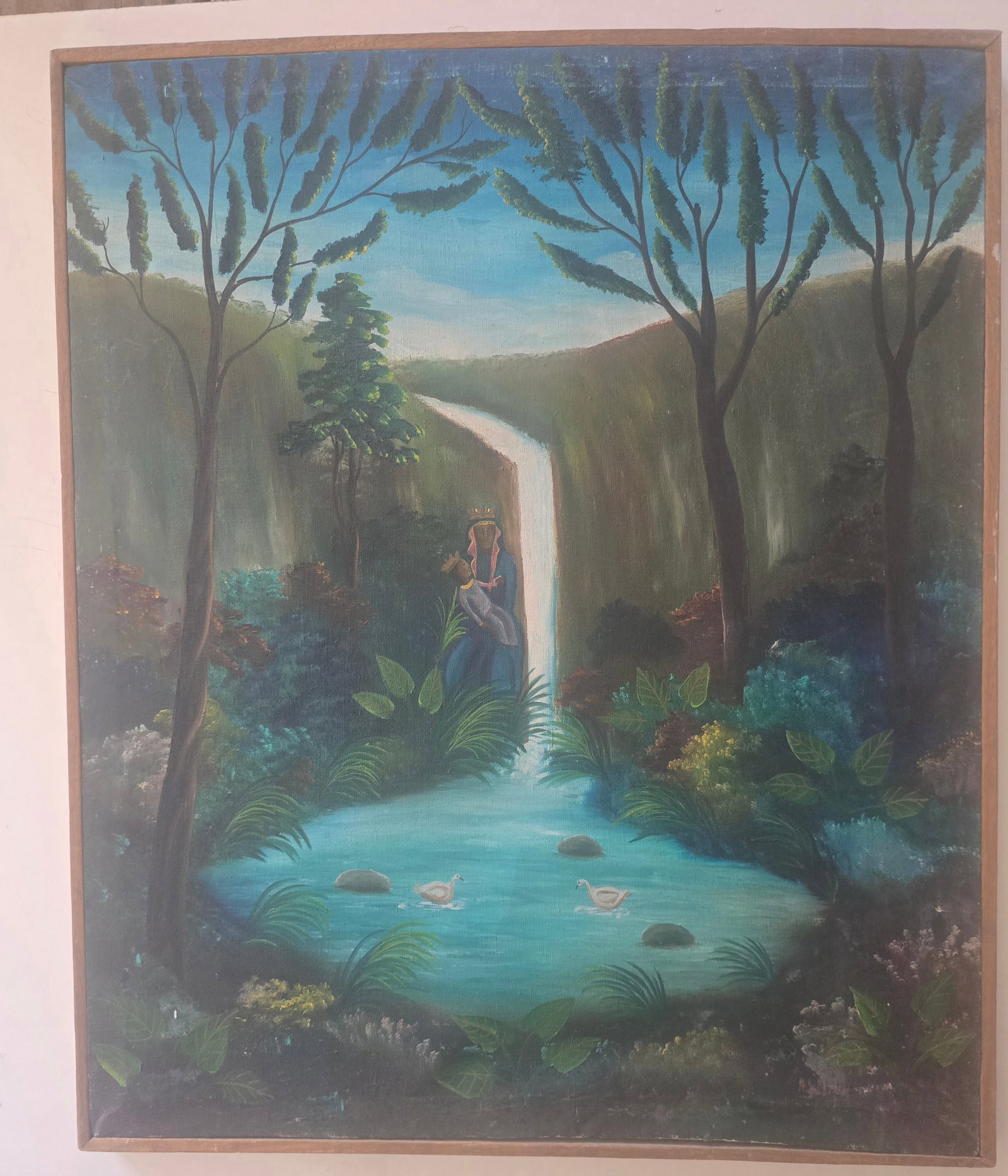 Haitian School (20th Century), Madonna and Child at the Waterfall, Oil on Canvas, Framed: This serene and spiritually evocative Haitian naive landscape depicts the Virgin Mary (crowned) holding the Christ Child beside a cascading waterfall that flows into a tranquil turquoise pool with swi
