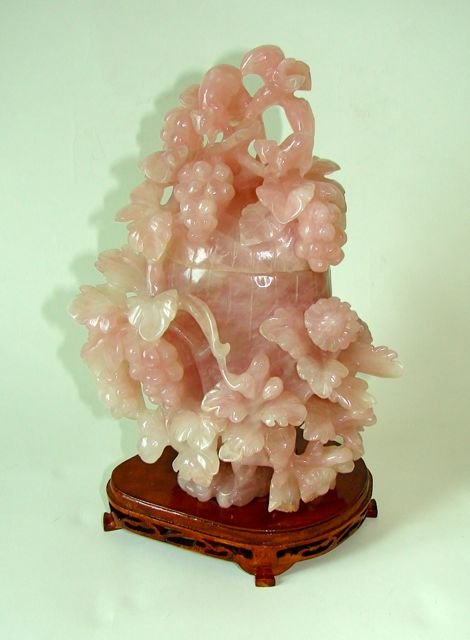 Chinese Rose Quartz Urn, H - 9.75.": Ornate carved rose quartz covered urn with fruit and floral garland. On a carved wood fitted base.