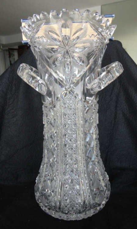 American Brilliant Cut Glass Two Handled Vase: Height - 14 inches, width - 6.5 inches. Unmarked, the vase has two handles, with floral,cane and hobnail cuts. The base has 24pt hobstar cuts.Appears to be in good condition with no chips to the teeth
