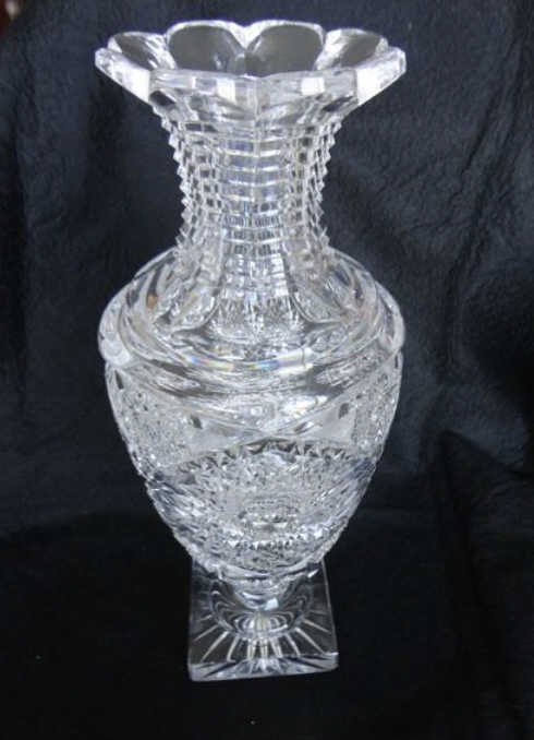 American Brilliant Cut Glass Footed Vase: Height - 12 inches. The vase has an urn shape with a scalloped rim, the neck is step cut and flared to a scalloped rim with four 24 pt hob cuts around the main body and small hobstar cuts surrounding 