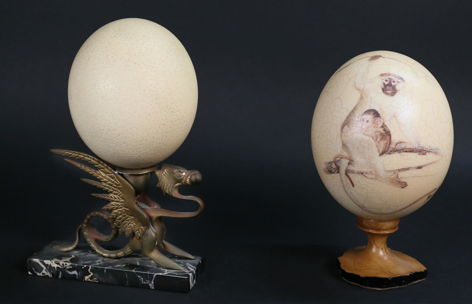 Two Decorative Ostrich Eggs: Two decorative ostrich eggs. 20th century. Painted ostrich egg on composite stand, ostrich egg on brass griffin on marble base. Painted ostrich egg signed illegibly. Wear and oxidization present on gr