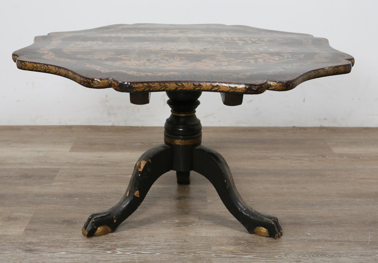 English Style Chinoiserie Lacquered Tea Table: English style Chinoiserie lacquered tea table. Octagonal form top, gilt painted Chinoiserie scene with decorated edges. Heavy loss to lacquer around tripod form base, legs and feet. Warping to wood on