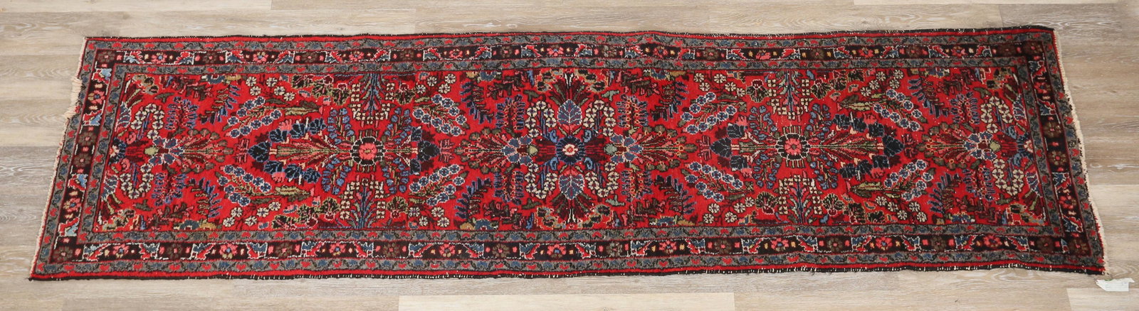 Persian Runner: Persian runner rug. Early to Mid 20th Century. Floral patterns and motifs against a scarlet red field, blue highlights in some flowers. Remnants of label on one corner. Wear to sides, loss to fringe o