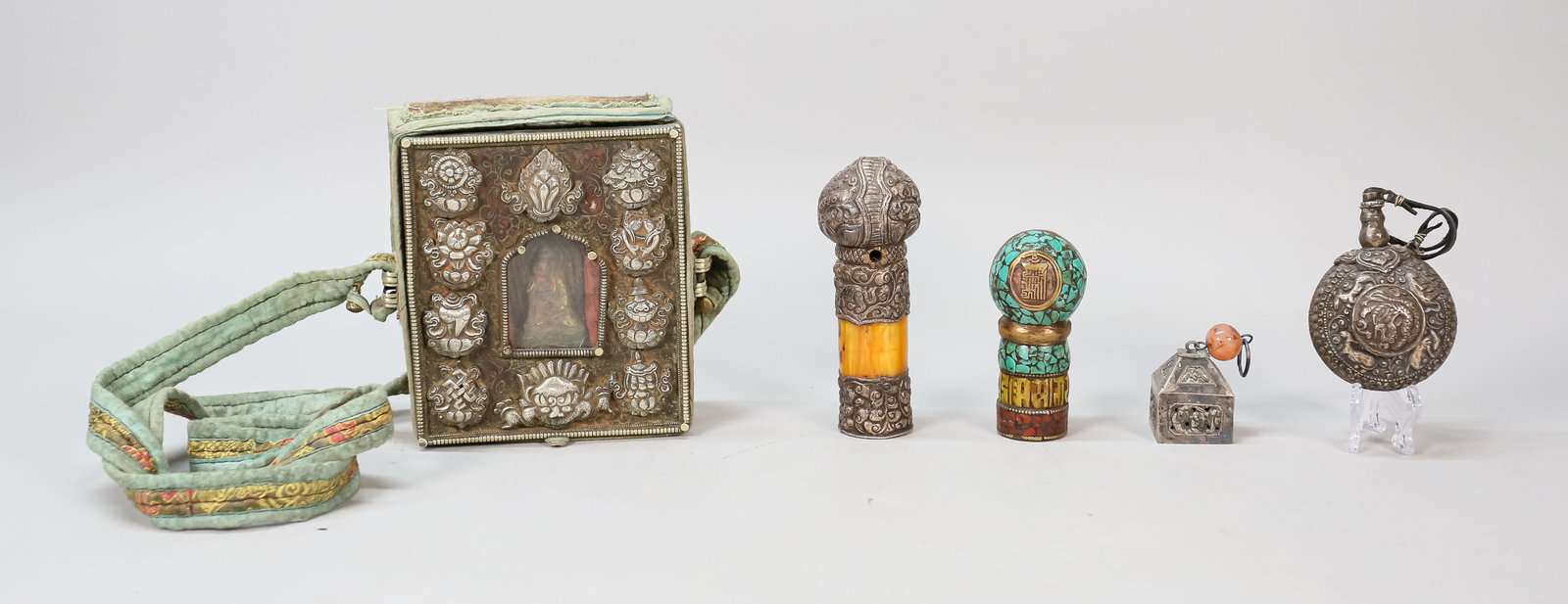 Grouping of Tibetan Items: Tibetan G'au prayer box with the 8 auspicious symbols, Buddha in a cloth carrying case. Repousse metal seal with amber. Hardstone carved seal. Repousse metal snuff bottle. Metal bell with carnelian st