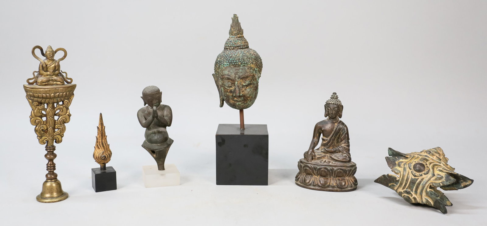 Grouping of Buddhist Sculptures: Grouping of 6 Buddhist sculptures. Thai patinated bronze Buddha head on stand. Burmese metal praying monk sculpture. Bronze Buddha Flame Siraspata sculpture on stand. Chinese bronze Buddha ornament. B