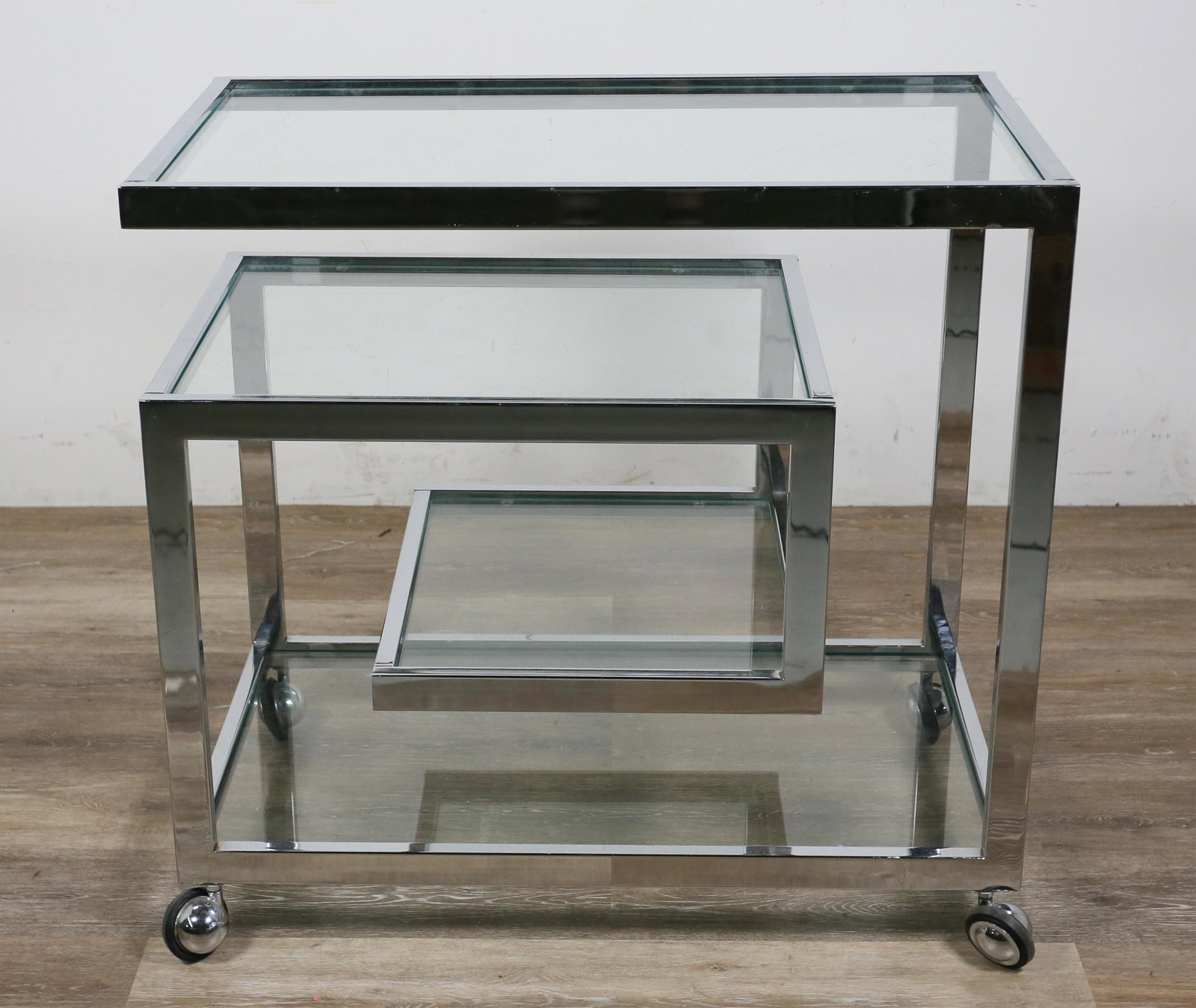Mid Century Modern Greek Key Form Chrome Bar Cart: Mid Century Modern Greek key form bar cart 20th century. Chrome frame in Greek key form with three graduated cantilevered glass shelves on casters. Casters marked "Shepherd". Chip to corner of lowest 