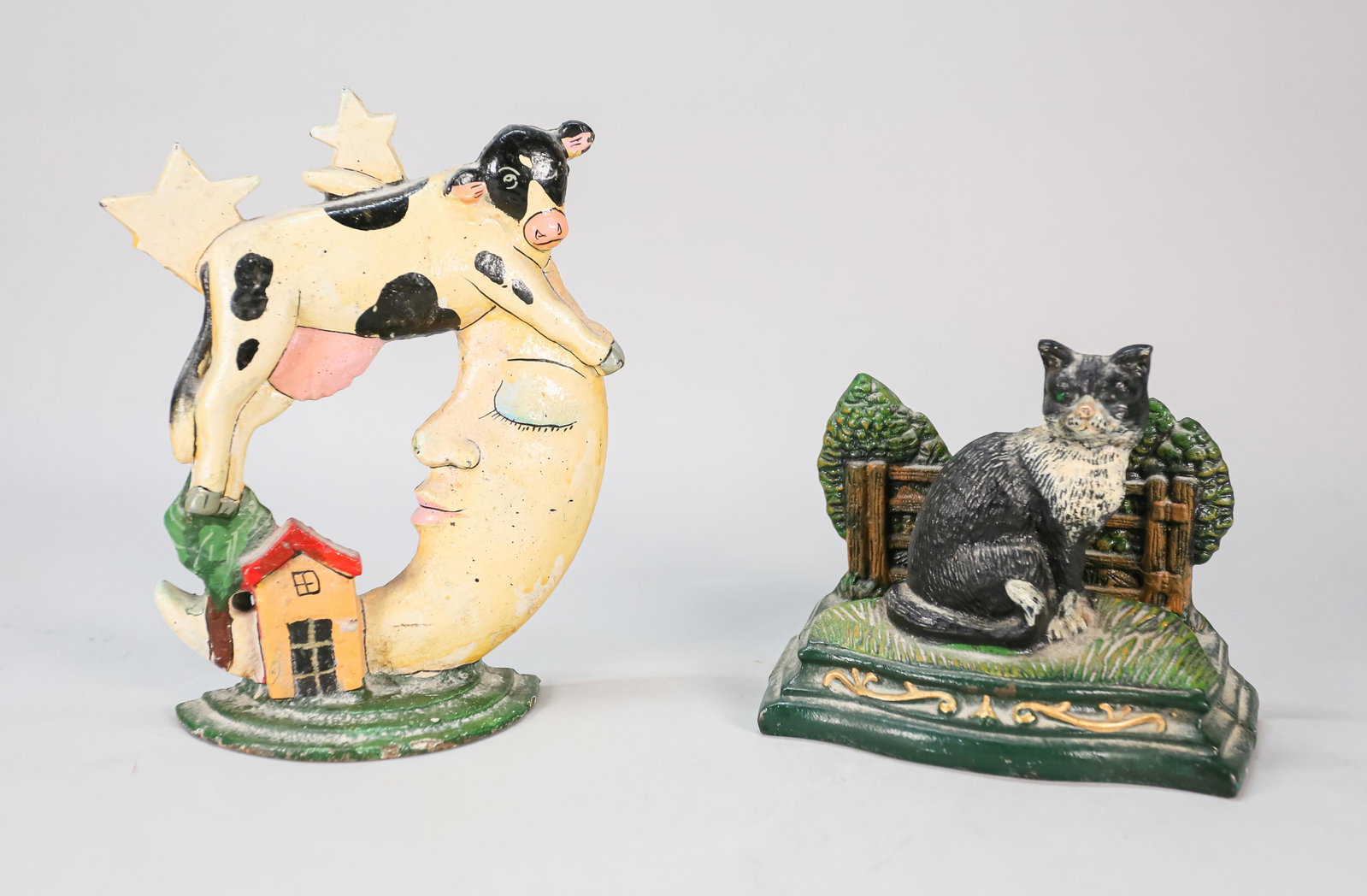 Two Cast Iron Folk Art Door Stops: Two cast iron folk art door stops. 20th Century. Painted cast iron door stop of sitting cat and cow jumping over the moon. Wear and losses throughout. Largest piece: 8 1/4" H x 6 1/2" L