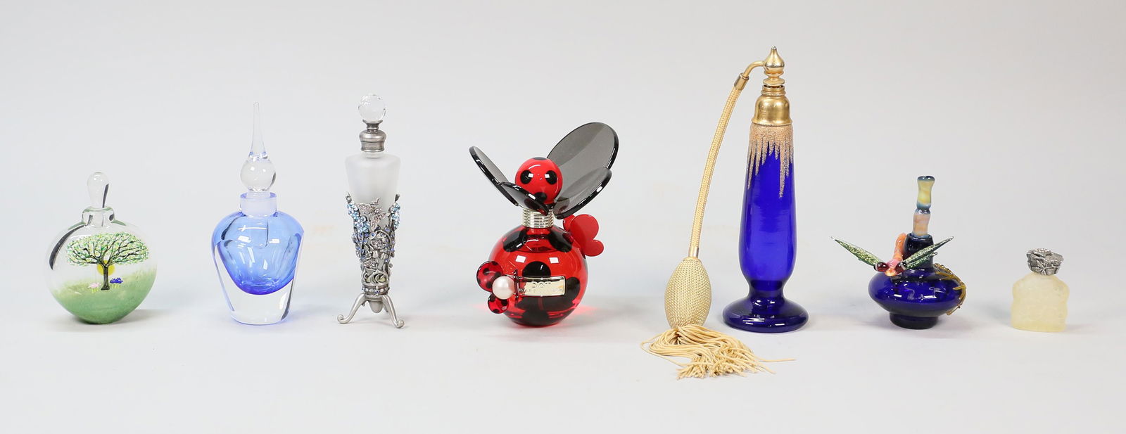 8 Art Glass Perfume Bottles: 8 perfume bottles, including 7 art glass bottles. Marc Jacobs Dot Lucite bottle, partially full; dragonfly bottle, signed illegibly; signed Matthew Buechner for Thames Glass tree bottle; blue bottle;
