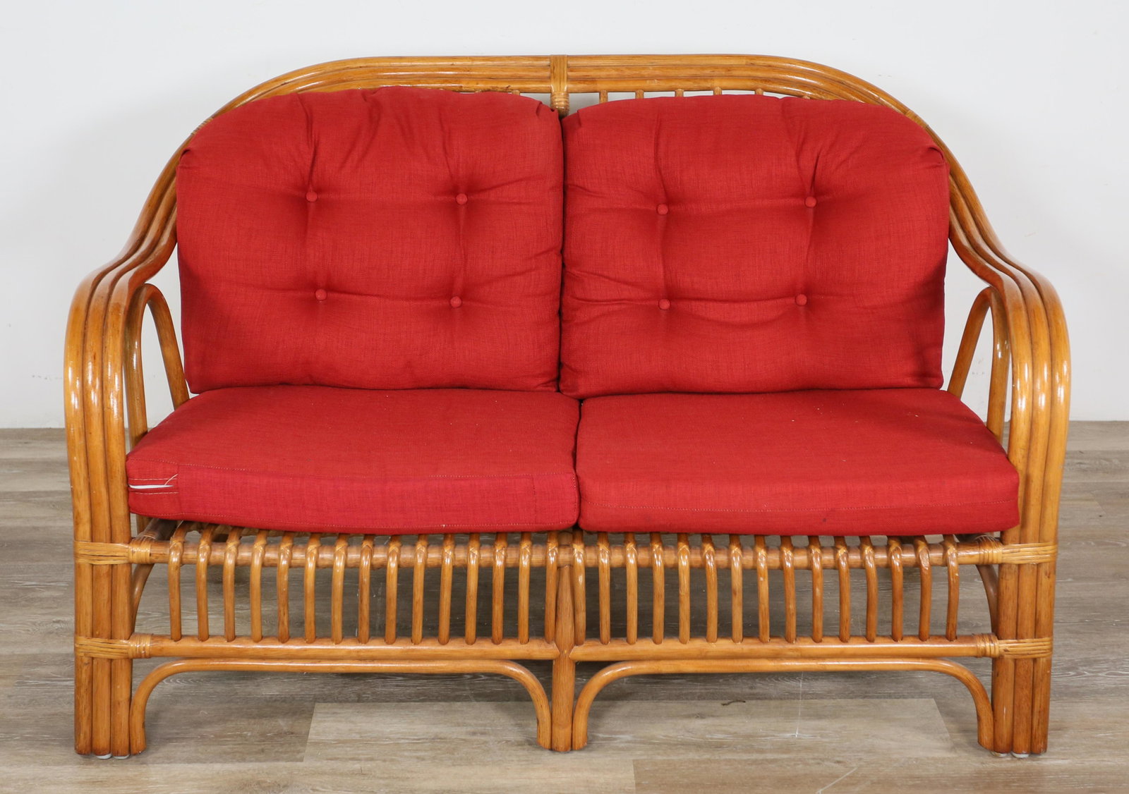 Mid Century Modern Bamboo Rattan Settee: Mid Century Modern bamboo rattan settee. 20th century. Bentwood rattan frame and four red cushions. White marks to top left corner of frame, indentations to wood on right side of top, some scratches a