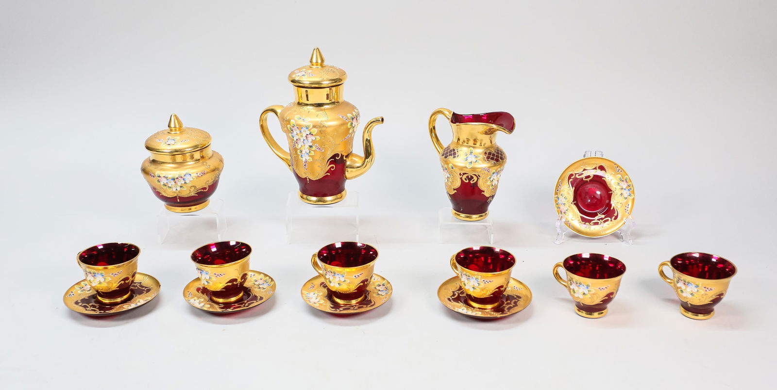 14 Piece Bohemian Glass Tea Set: 14 piece Bohemian glass tea set. Cranberry glass with gilt and enameled floral decoration. Teapot, creamer, sugar, 6 tea cups and 5 saucers. Wear and light scratches around neck of tea pot, chips to e