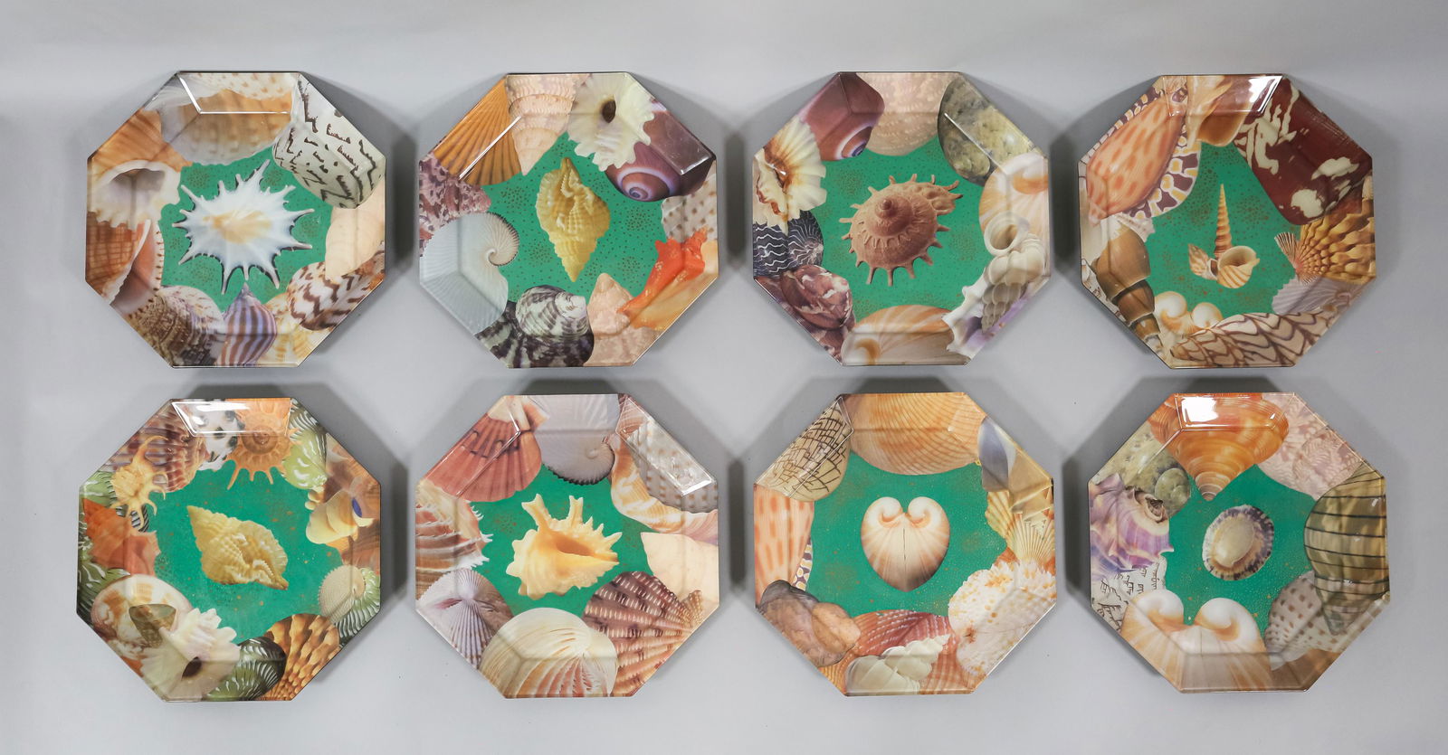 8 Pablo Manzoni Glass Seashell Octagonal Plates: Pablo Manzoni (Italy / American, New York, 1939-2022). 8 octagonal glass plates with collage designs and painted backs. All with seashell motifs on a green ground. All signed Pablo Manzoni N.Y.C. on t