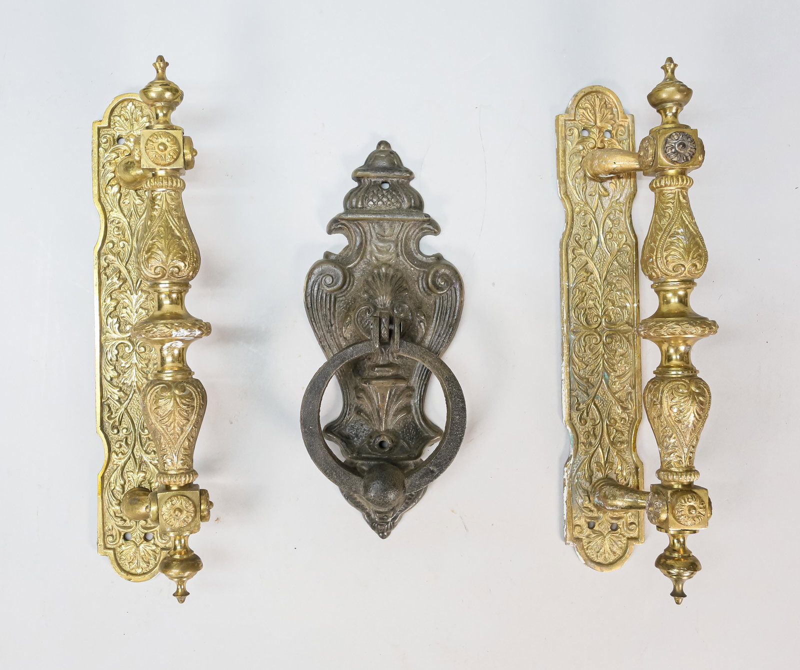 3 Architectural Elements: Pair of brass door handles. 1 iron figural door knocker. Brass door handles have rust present to the back. 1 brass door handle: 12" H x 2" W x 2" D.From the estate of artist Stanley Lindwasser.