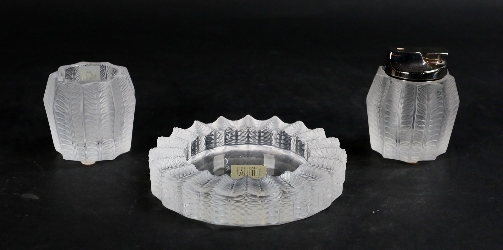 3 Piece Lalique France Jamaique Smoking Set: 3 signed Lalique Jamaique smoking accessories. Ashtray, 5 1/2"-diameter; cigarette holder, 2 3/4"H and lighter, 3 1/4"H. All signed Lalique France with additional paper labels.