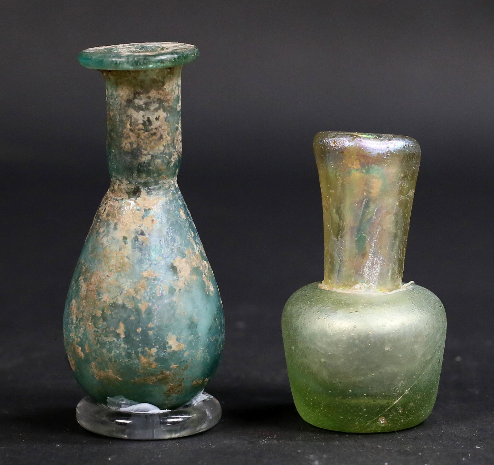 2 Roman Glass Unguentarium: 2 Roman green glass unguentarium. 3"H and 2"H. Some wear to both.