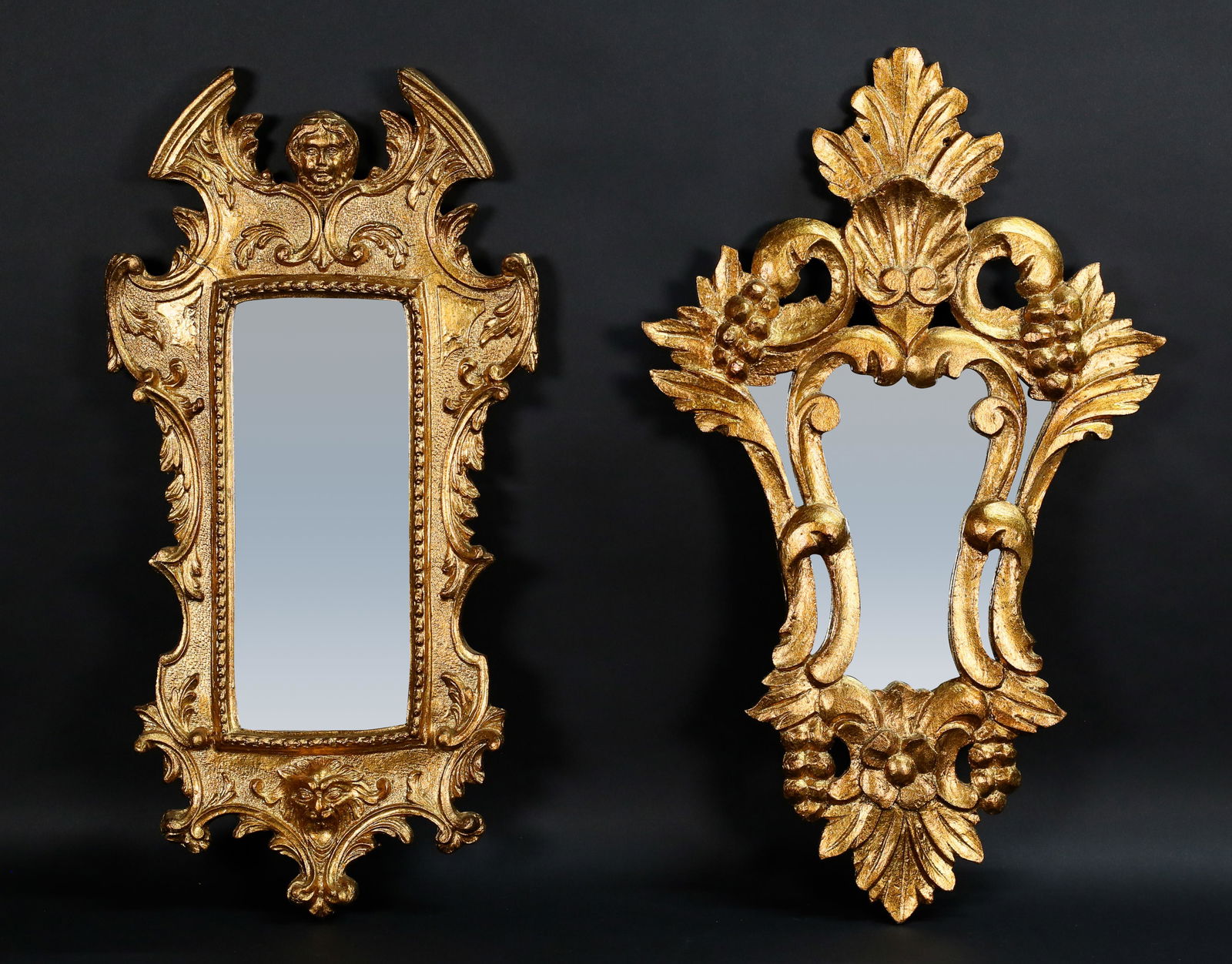 2 Carved Giltwood Mirrors: 2 carved gilt wood mirrors, grape and leaf, and figural with woman's and lion's heads. Grape and leaf mirror with Made in Spain label. Figural mirror 24 3/4" x 12 1/2". Split to wood on upper left sid