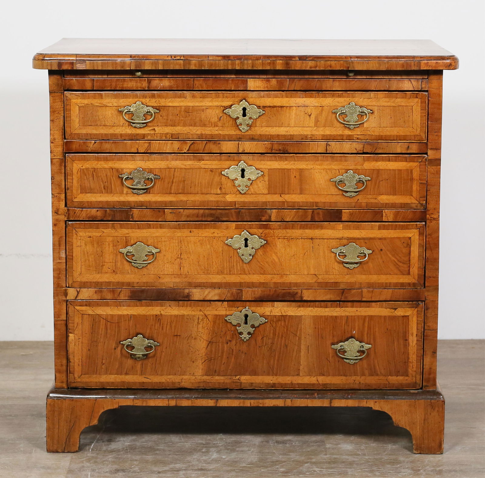 Queen Anne Walnut Chest of Drawers: Queen Anne walnut chest of drawers. Circa 1710. Four graduated drawers, brushing slide, bracket feet. Later brass hardware. Wear, scratches, nicks, and scuffs to wood on top of chest. Losses to veneer