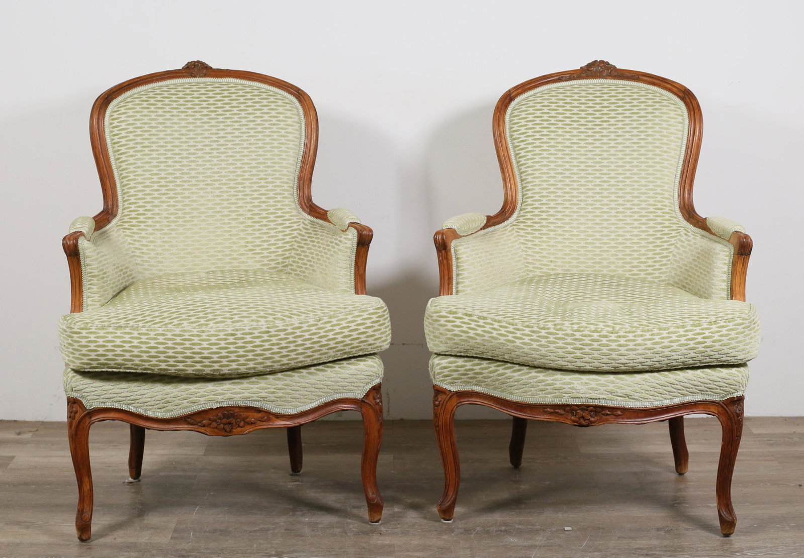 Pair of Louis XV Style Bergere Armchairs: Pair of Louis XV style bergeres (closed armchairs). 19th century. Carved walnut, cabriole legs, later upholstery and cushions. Relining to underside of chairs. Wear, nicks, chips, and marks throughout