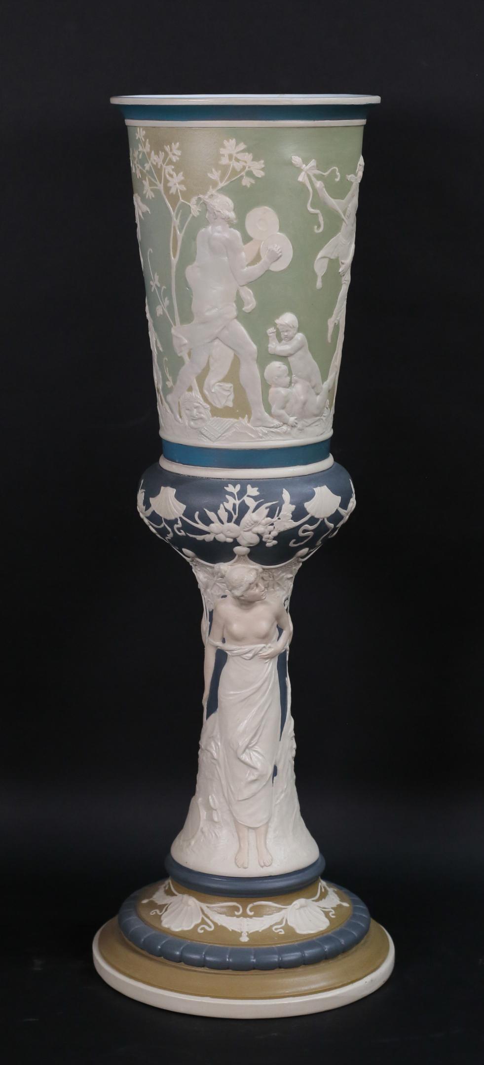 Mettlach Jasperware Pedestal Vase: Mettlach jasperware porcelain pokal / pedestal vase. Allegorical scenes in relief. Incised mark on the underside Mettlach 2418. 22"H x 6 1/2"-diameter at top. Some discoloration and scratches to inter