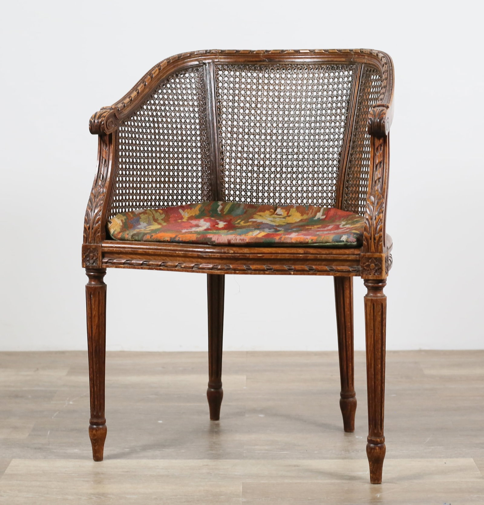 Louis XVI Style Caned Armchair: Louis XVI style caned armchair. Early 20th century with later seat pad. Reeded legs and caned back and seat. Scratches, marks and scuffs throughout wood of chair. Wear and losses to threading of seat 