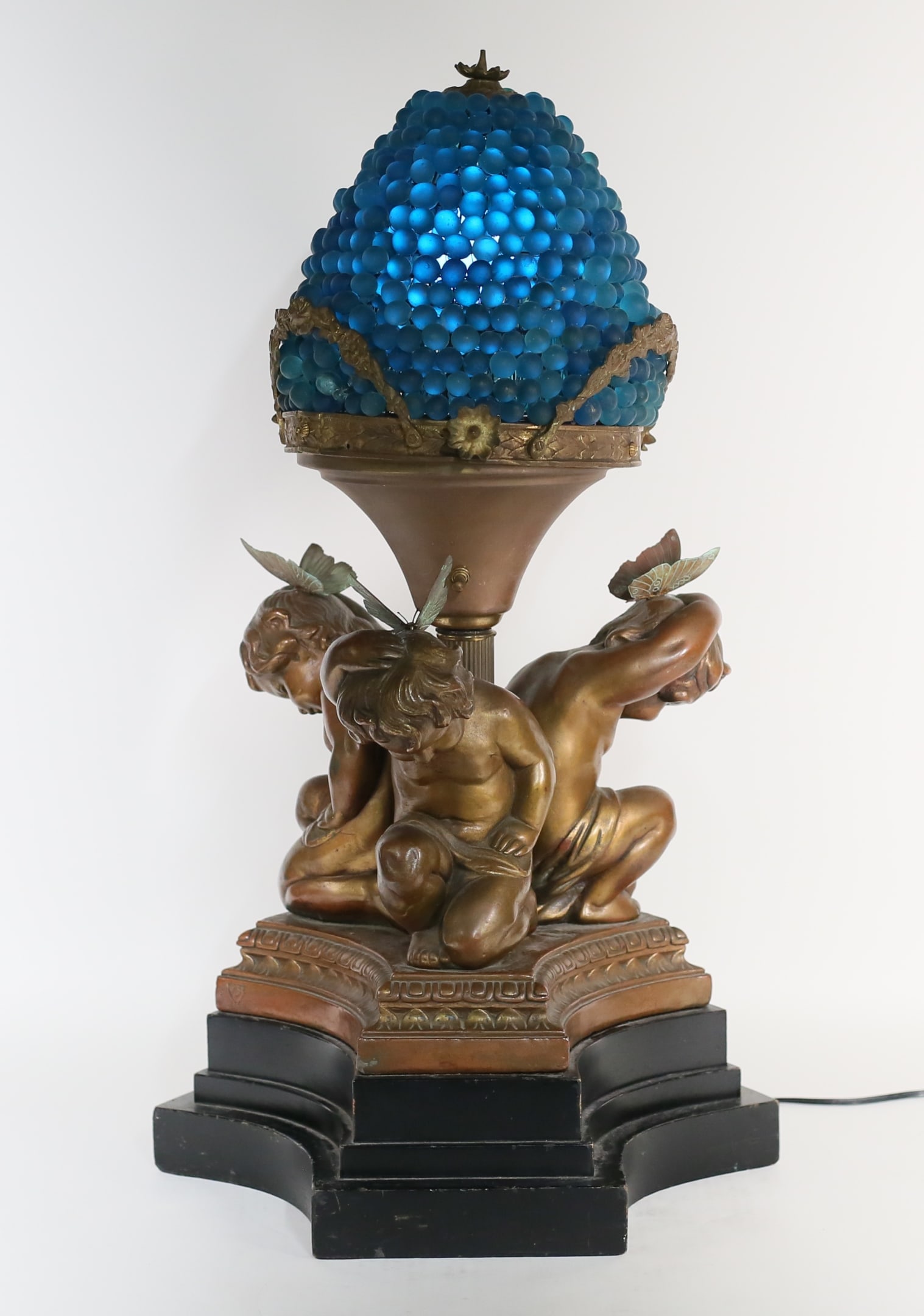 Armor Bronze Clad Cupid Lamp Glass Grapes Shade: National Metalizing Company "Armor Bronze" bronze clad figural Cupid lamp. With a blue glass grape shade. Later butterflies added to Cupids' heads. Mounted on a wooden base. Armor Bronze and copyright