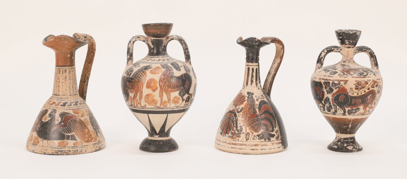 4 Greek Style Pottery Vessels: 4 Greek style terracotta pottery vessels. 2 amphorae / vases, both black figure with animal motif, larger 6 1/4"H; 2 oinochoe / wine vessels, larger 5 3/4"H. Larger amphora repair to handle and chip a