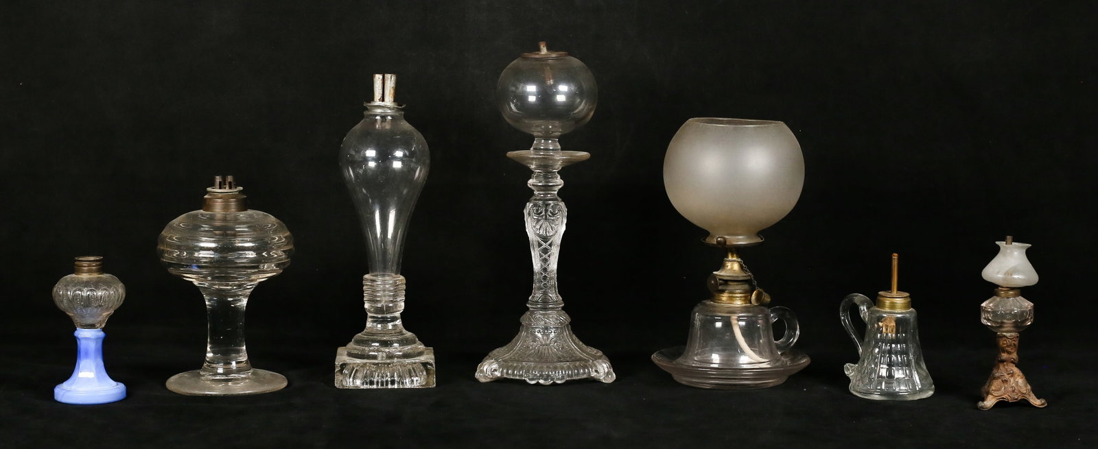 7 Miniature Whale Oil Lamps: 7 miniature oil lamps. Some are pressed glass and some are blown glass. Pressed glass may be Sandwich glass. Some appear to have original burners. Nicks, chips and cracks. Tallest 11 1/2"