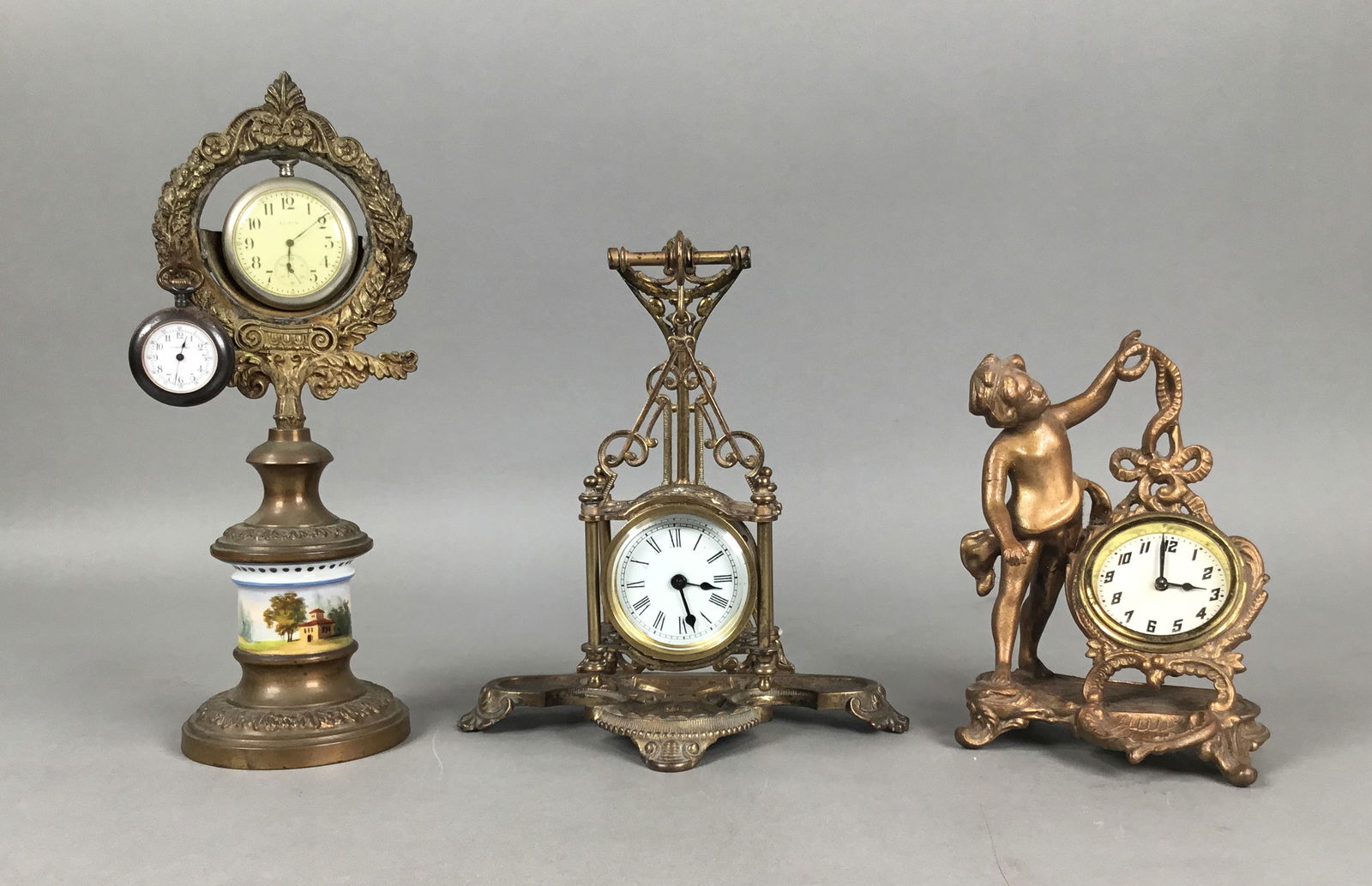 3 Desk / Table Clocks: 3 desk / table clock. Hanging clock, 7 3/4"H; clock on figural cherub stand, clock marked Made in USA, 6 3/8"H; porcelain and brass pocket watch clock / holder with two watches, larger Elgin, smaller