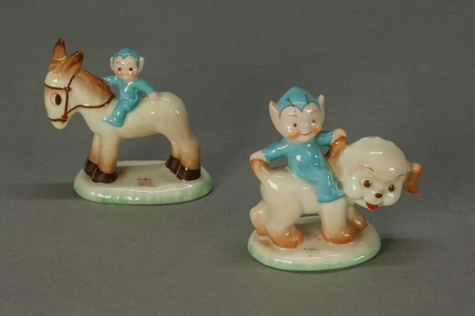 2 Mabel Lucie Atwell Shelley Porcelain Figurines: 2 Shelley English bone china Boo Boo pixie figurines, based The Boo-Boos by Mabel Lucie Atwell. Each signed Mabel Lucie Atwell on the base. Donkey 2 7/8"H, puppy 2 3/4"H.