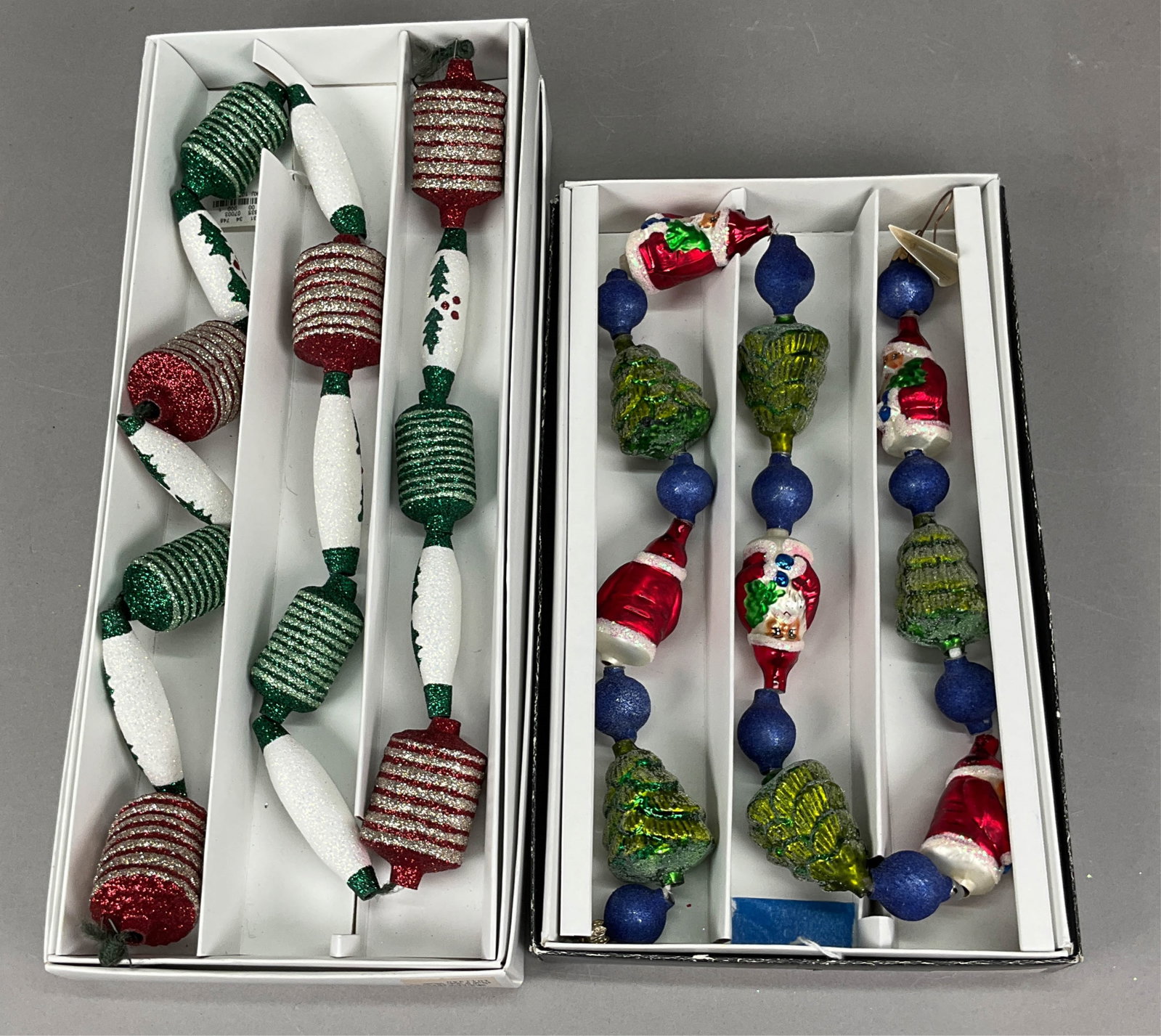 2 Radko Christmas Garland with Tags/Boxes: 2 Radko Christmas Garland with Tags/Boxes. Includes Green Red Holly Berry Garland -- 45" long, & Santa Claus Christmas Tree Garland - 36" long. Some paint and glitter loss.Ornament stands are NOT INCL