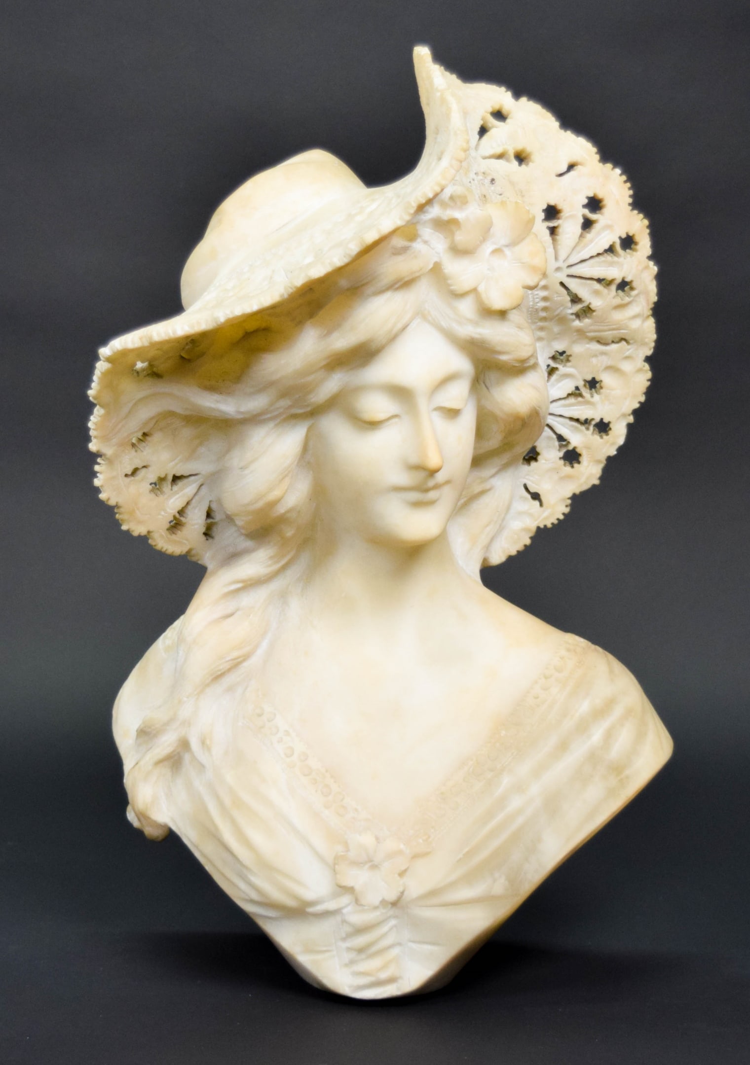 Carved Alabaster Bust of a Woman: Carved alabaster bust of a woman. Unsigned. 15 5/8"H. No base. Chips to edges of hat and flower chips and flakes to shoulders.