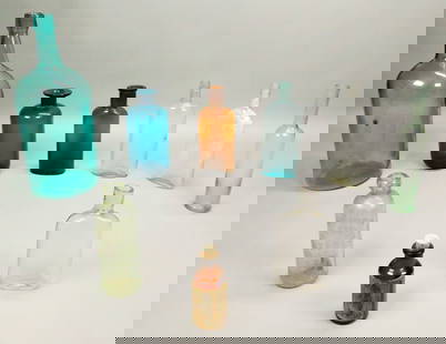 9 Vintage Glass Bottles: Lot of 9 vintage colored glass bottles. Tallest 14 3/4"H. Largest bottle crack to the underside, Trommer imperfections to the neck, W.H. Cawley chips to the rim and chip to one side, losses to paper l