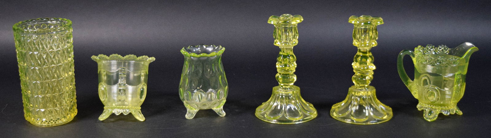 6 Pieces Vaseline Glass: 6 pieces Vaseline / uranium glass. Pair candlesticks, vase, thumbprint vase, sugar and creamer. Larger vase 7"H x 3 3/4"-diameter at top. Candlesticks both with chips to candle holders, chips and roug