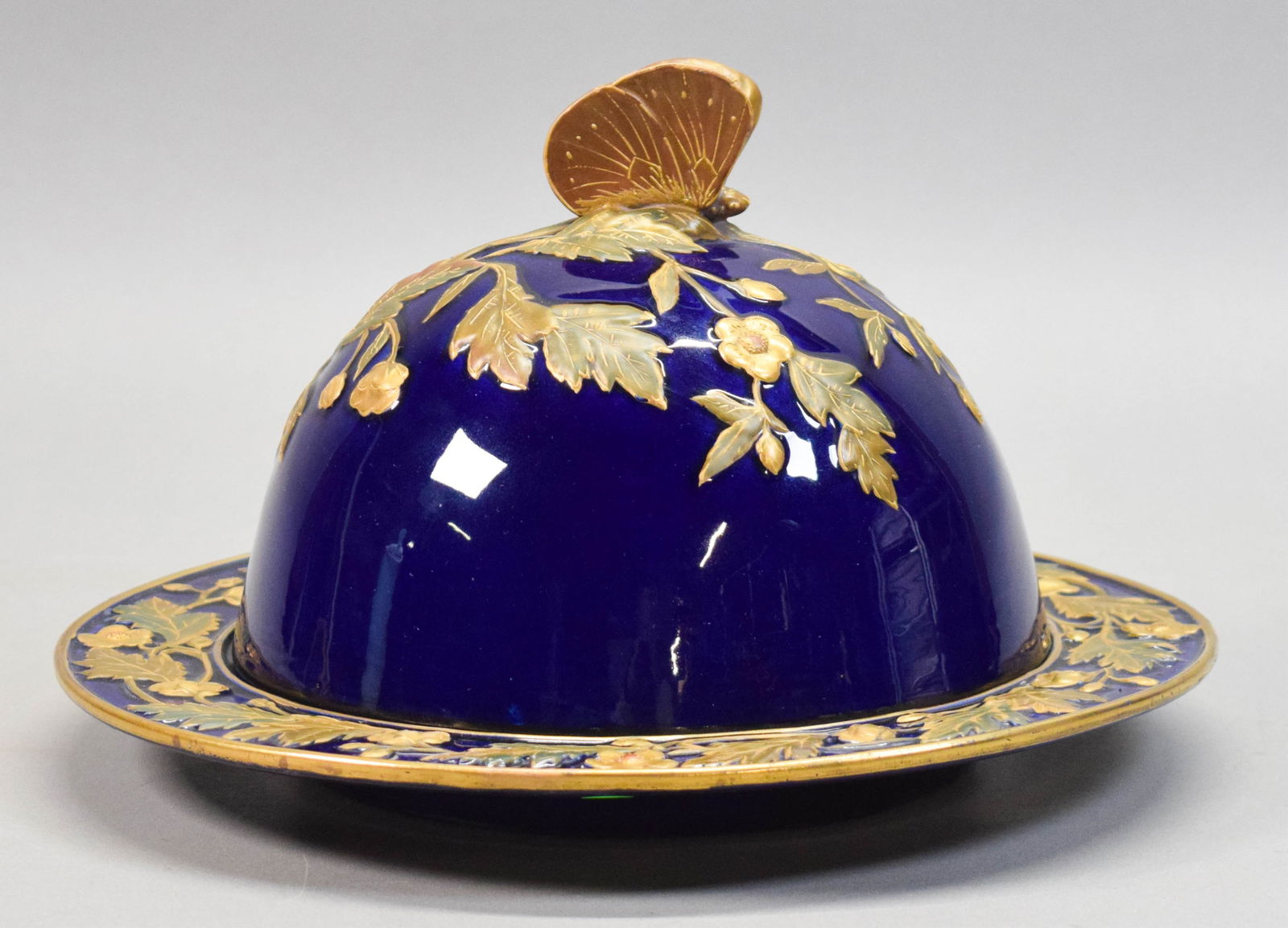 George Jones Majolica Muffin Dish: George Jones majolica porcelain muffin dish. Dome and underplate, cobalt blue with gilt painted floral decoration and butterfly finial. Partial mark on the underside. 7 1/4"H, underplate 11 5/8"-diame