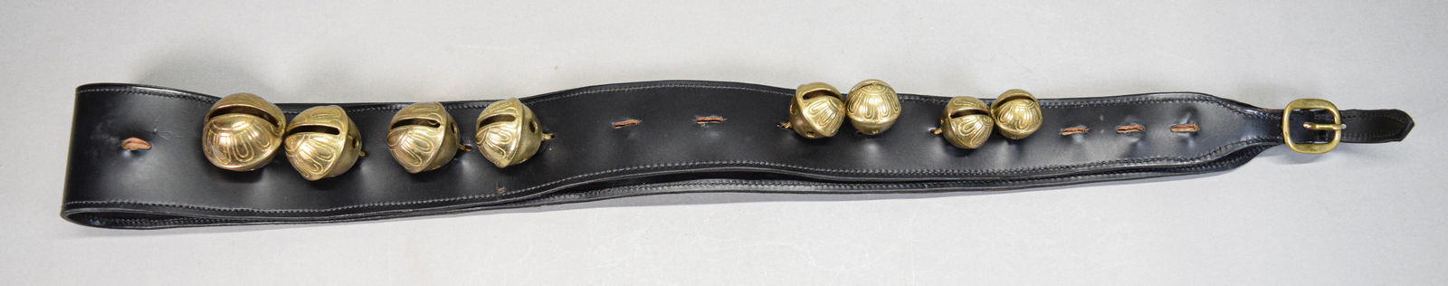 Set of Brass Sleigh Bells: Set of brass sleigh bells on a leather strap. Unmarked. 82 1/4"L. With 23 of 29 bells (missing 6 bells), 15 bells detached from strap. Tear to leather at one notch, wear to leather at holes.