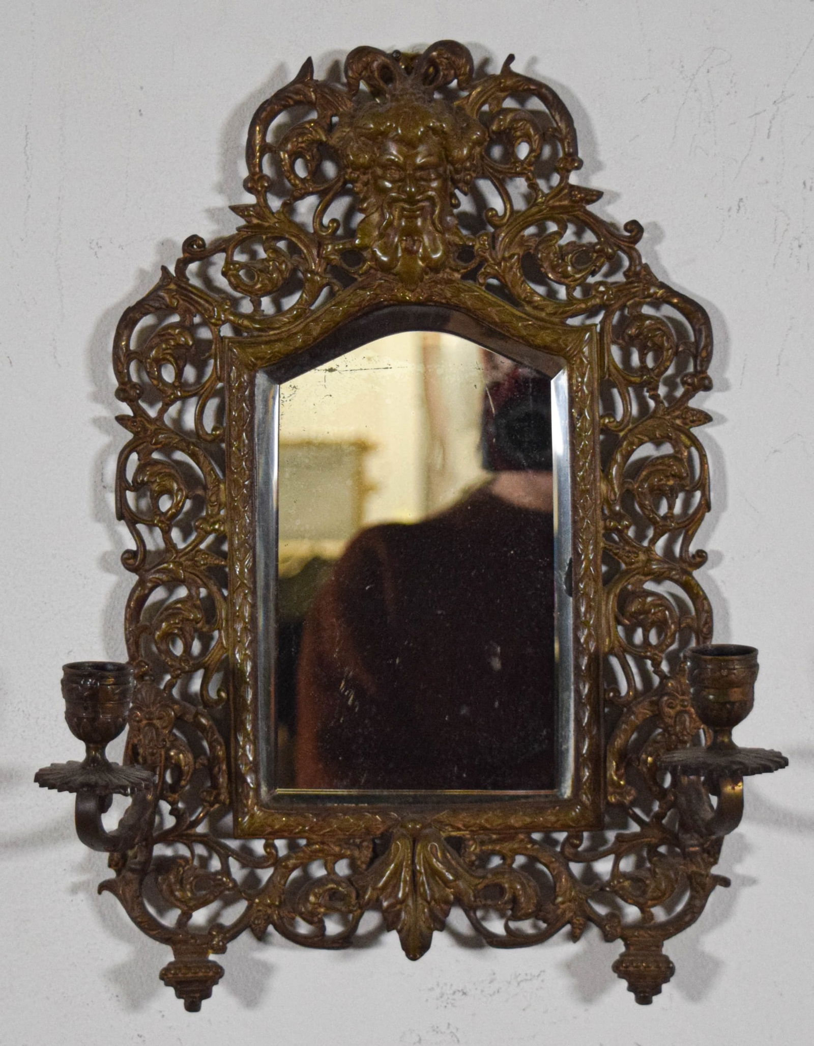 Brass Bacchus Mirrored Wall Sconce: Brass mirrored two light hanging wall sconce, with Bacchus head. Unsigned. 14 1/2"H x 11 1/4"W. Chips and scratches to glass.