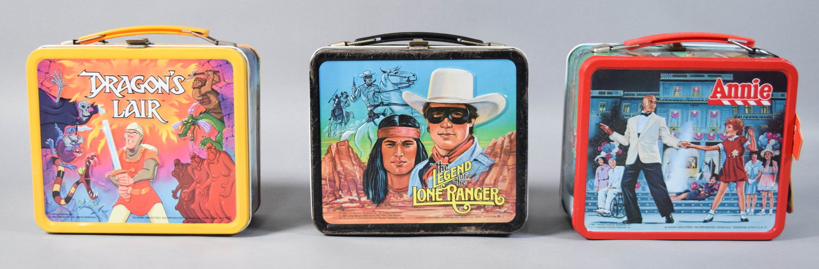 3 Aladdin Industries Lithographed Metal Lunchboxes with Thermoses: Three vintage lithographed metal lunchboxes with matching insulated thermoses, manufactured by Aladdin Industries. The collection includes a 1983 yellow-framed Dragonâ€™s Lair set, a 1980 blac